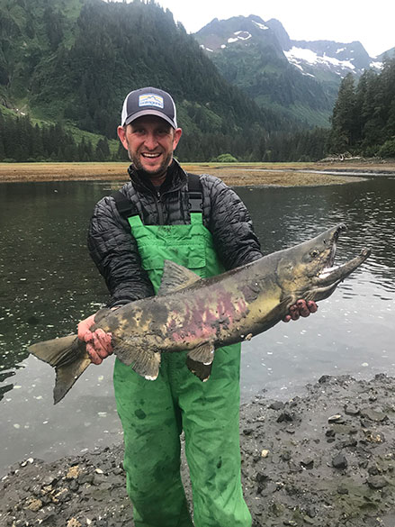 Will Morby standing in front of a lake holding a large fish.